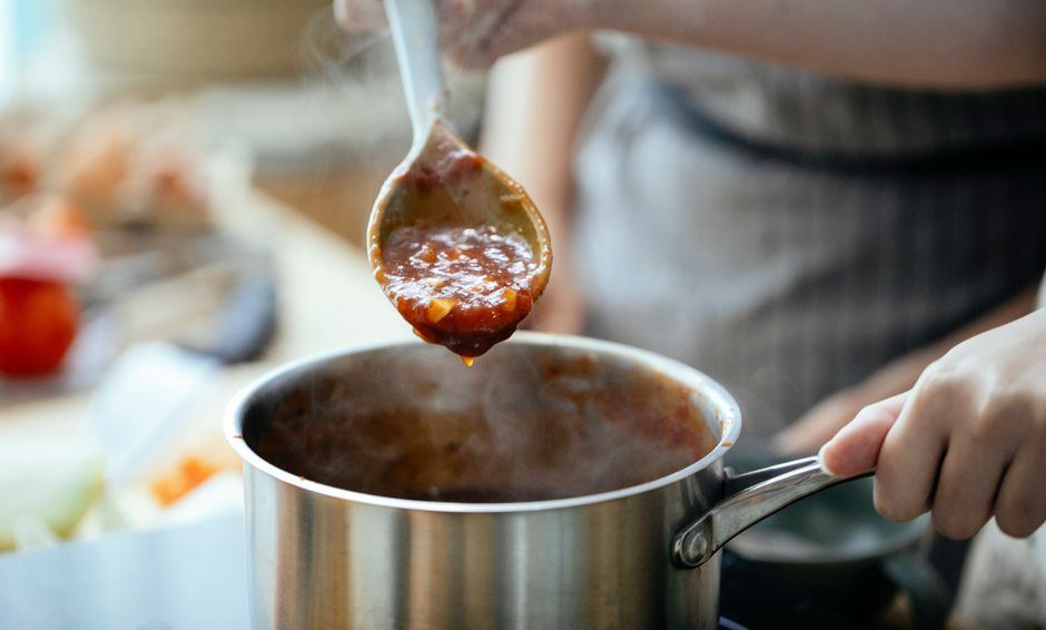 Crop anonymous females in aprons cooking sauce for pasta in saucepan in kitchen together